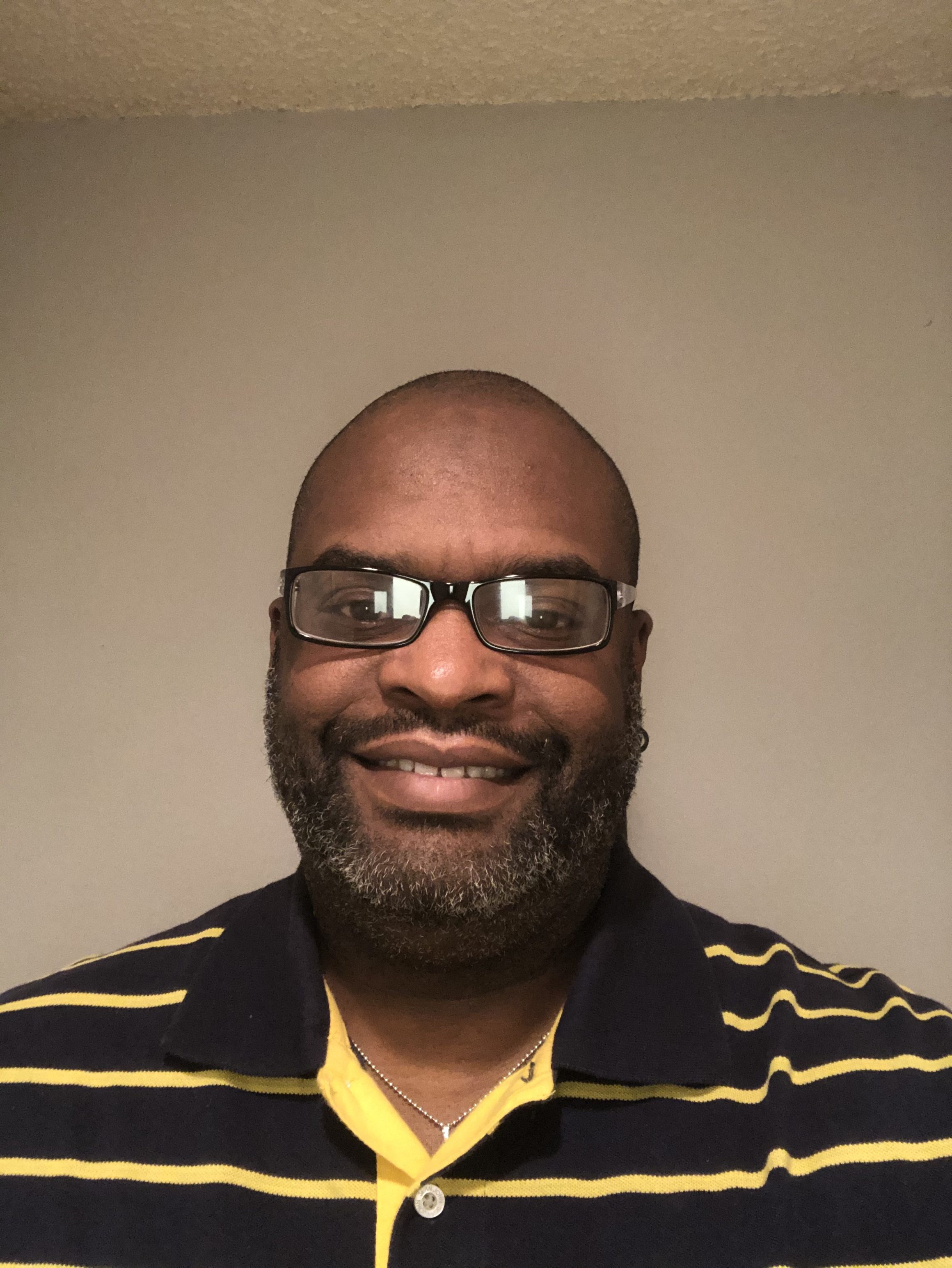 Closeup picture of black man smiling wtih glasses and black and yellow striped polo shirt 