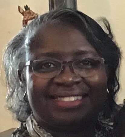 Closeup picture of black woman smiling with glasses and grey hair 