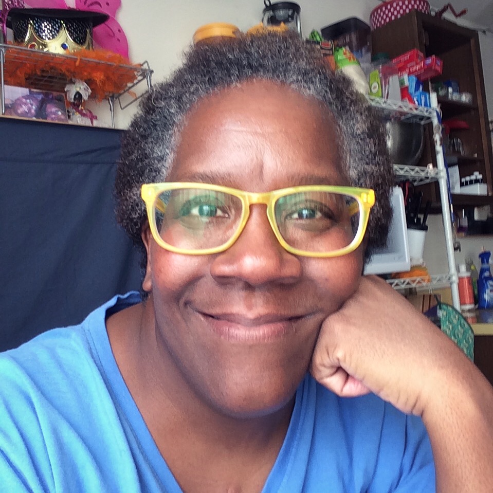 Closeup picture of black woman smiling with blue shirt and yellow glasses 